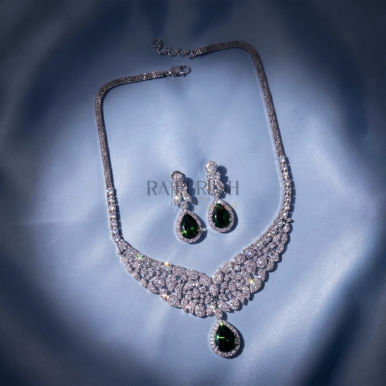 Stunning round brilliant moissanite tennis necklace featuring green sapphire pear cut diamond alternative teardrop clusters on a luxurious blue silk background.