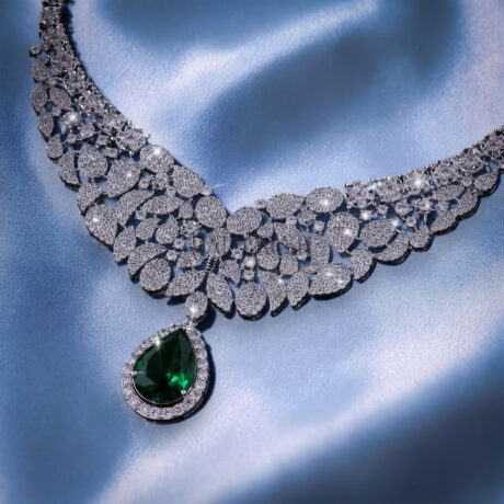 Stunning round brilliant moissanite tennis necklace featuring green sapphire pear cut diamond alternative teardrop clusters on a luxurious blue silk background.
