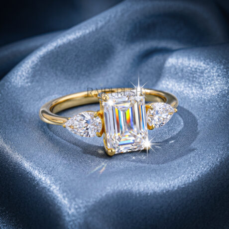 Elegant emerald-cut moissanite engagement ring with pear-shaped side stones, finished in 14k yellow/rose gold plating.