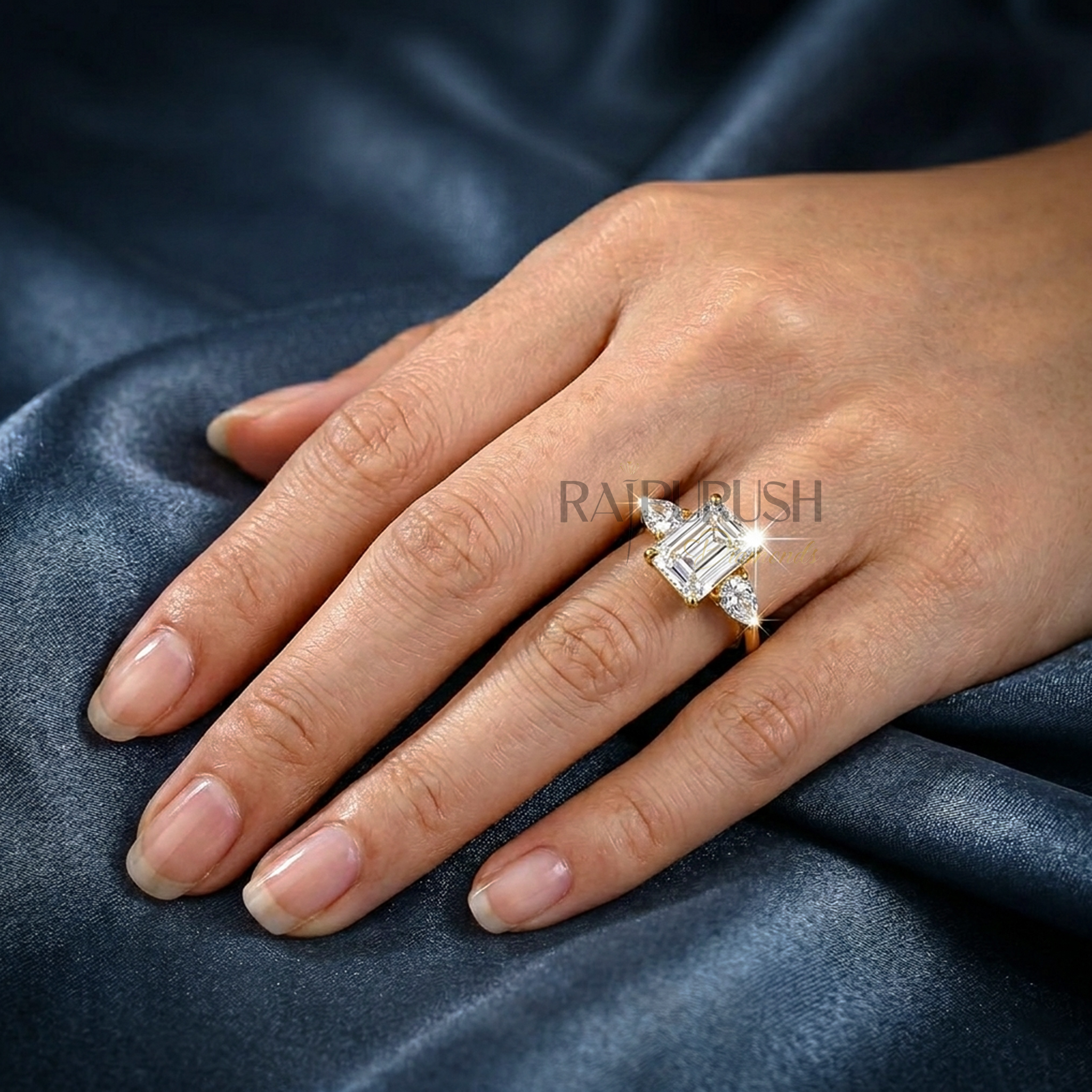 Elegant emerald-cut moissanite engagement ring with pear-shaped side stones, finished in 14k yellow/rose gold plating.