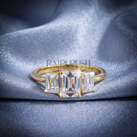 Classic three-stone engagement ring featuring a central emerald-cut moissanite flanked by two emerald side stones, finished in 14k yellow/rose gold plating.